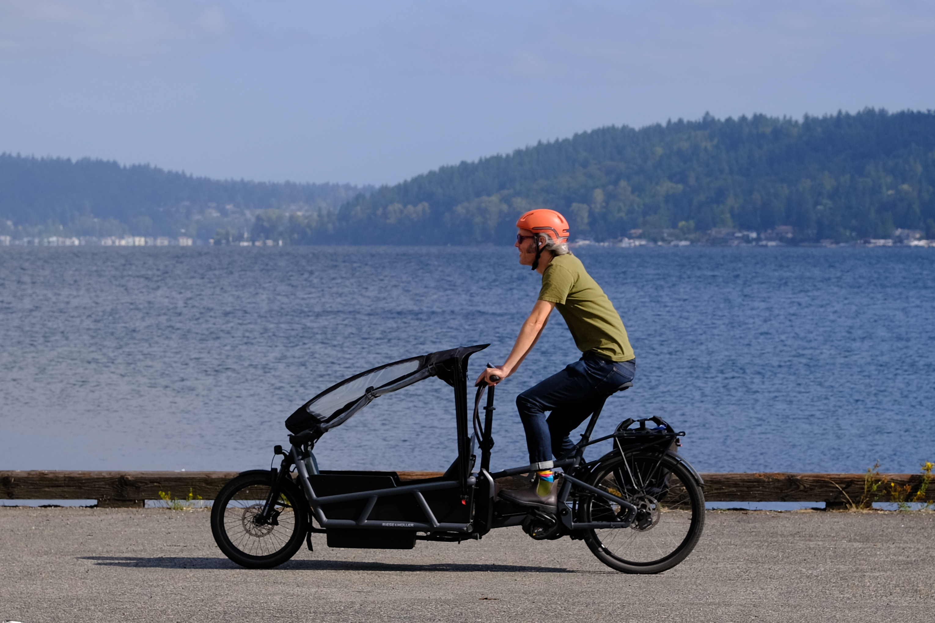 A man riding a Riese & Müller Load4 75 cargo bike with Lake Washingtion, Seattle, behind.